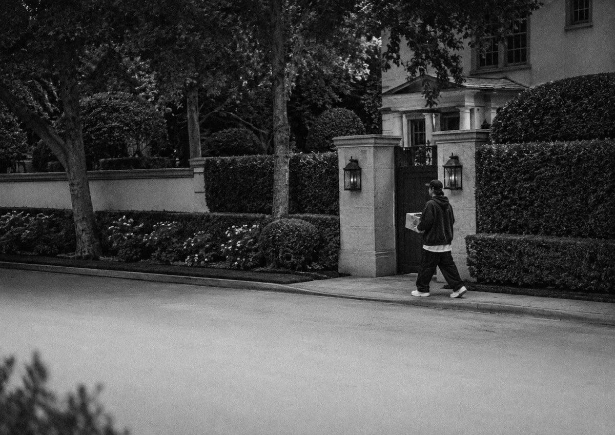 A person walking past a gated estate entrance on a residential street.